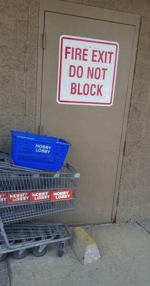 door with sign reading 'fire exit do not block' is blocked by a brick and a row of shopping carts